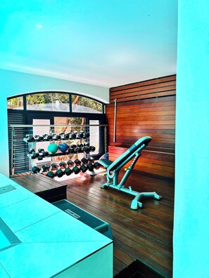 A gym with exercise equipment, a wall-mounted rack of dumbbells, and a wooden wall. - Stylish 2-Bed Apartment with Pool, Gym & Mountain Views. Walk to V&A Waterfront! (Cape Town)