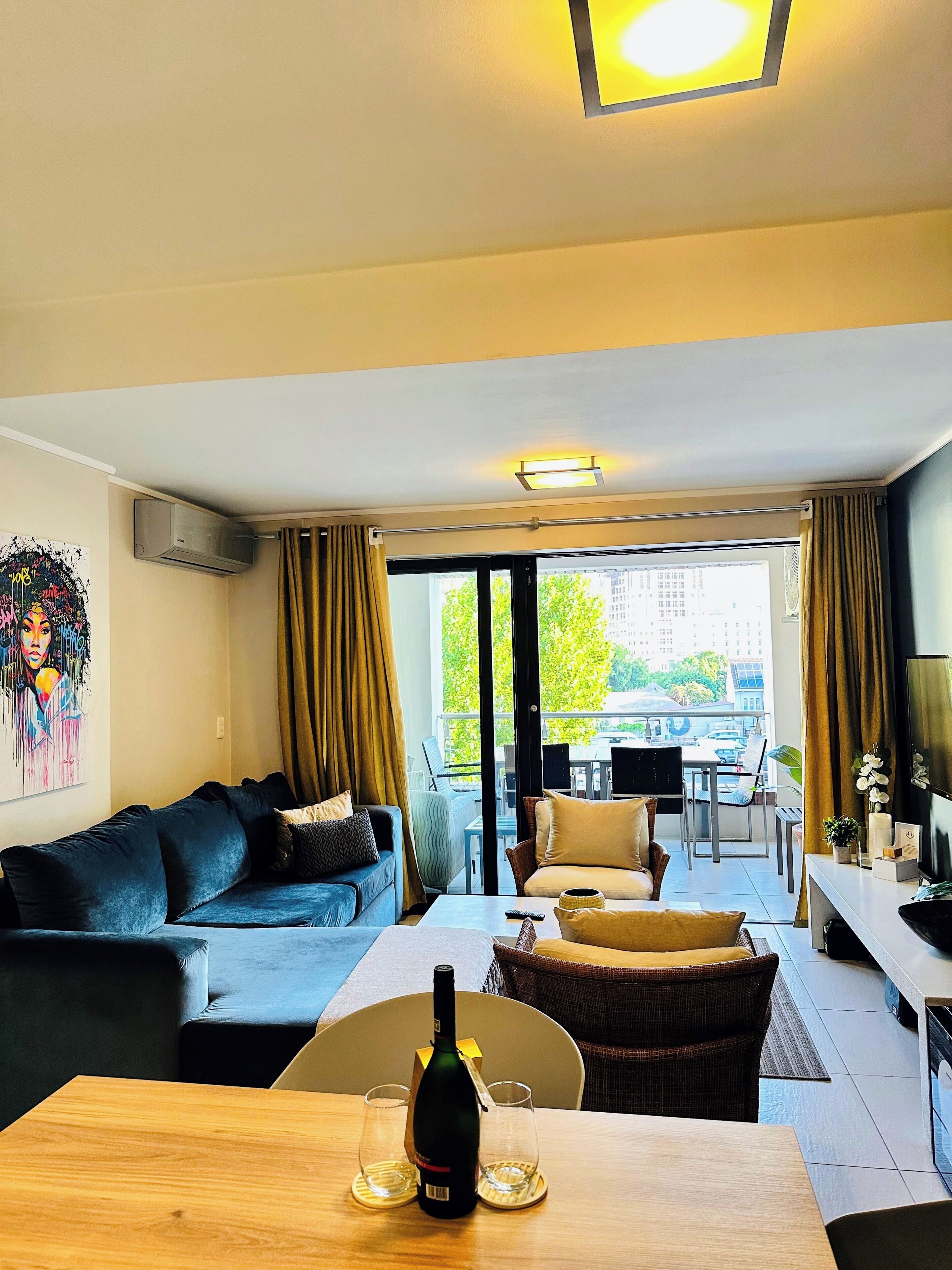 A modern living room with a sofa, a dining table with a bottle and glasses, a TV, and a balcony with outdoor furniture.