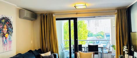 A modern living room with a sofa, a dining table with a bottle and glasses, a TV, and a balcony with outdoor furniture.