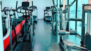 A gym with exercise equipment, large windows, and a red accent wall. - Stylish 2-Bed Apartment with Pool, Gym & Mountain Views. Walk to V&A Waterfront! (Cape Town)