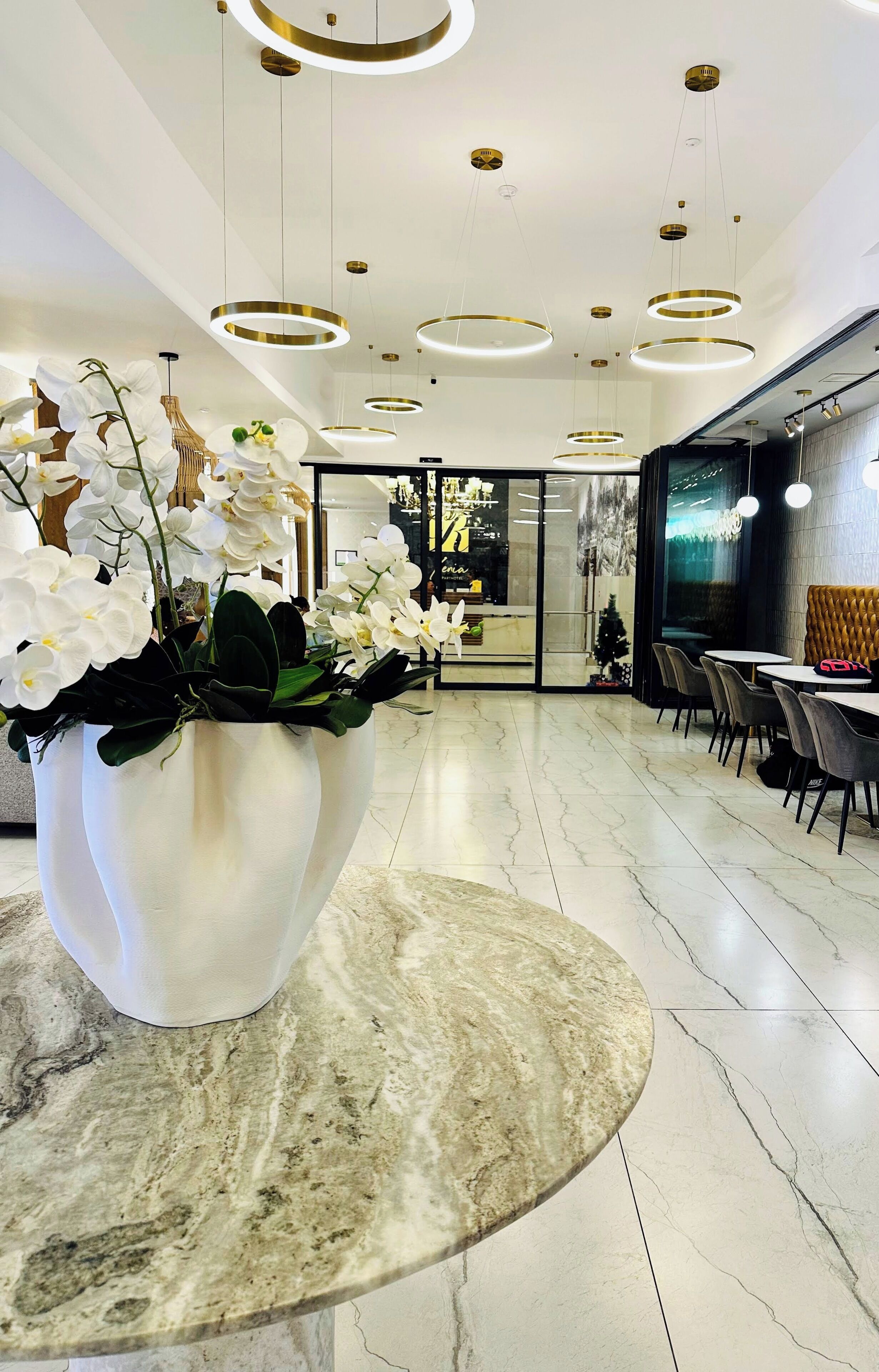 A modern interior with a marble floor, a large white vase with white flowers, and a seating area with tables and chairs.