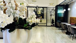 A modern interior with a marble floor, a large white vase with white flowers, and a seating area with tables and chairs. - Stylish 2-Bed Apartment with Pool, Gym & Mountain Views. Walk to V&A Waterfront! (Cape Town)