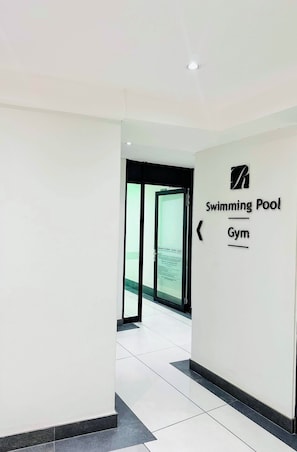 A hallway leading to a swimming pool and gym area with a sign indicating the facilities. - Stylish 2-Bed Apartment with Pool, Gym & Mountain Views. Walk to V&A Waterfront! (Cape Town)