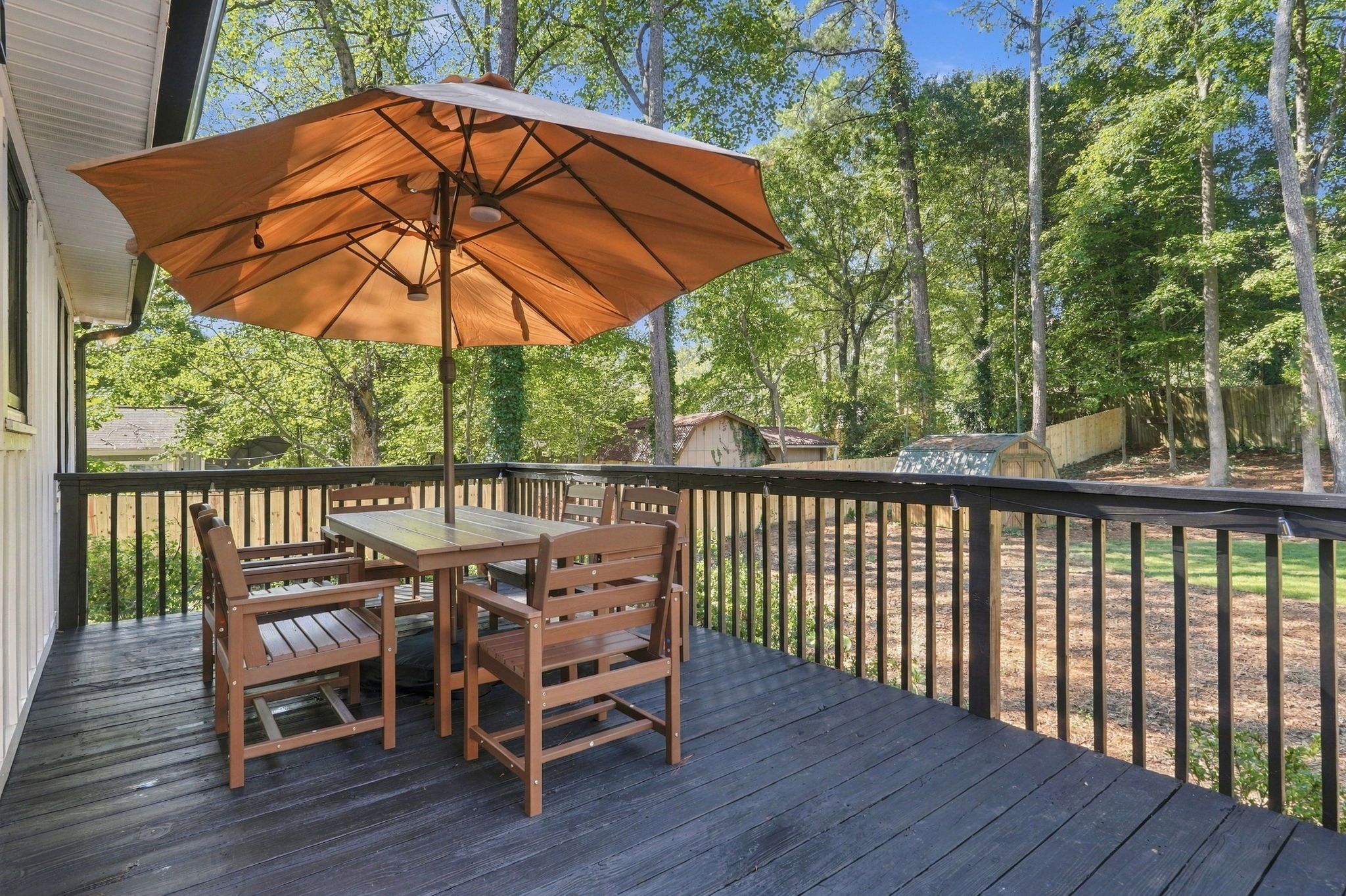 A wooden deck with a table and chairs, an umbrella, and a view of a wooded area.