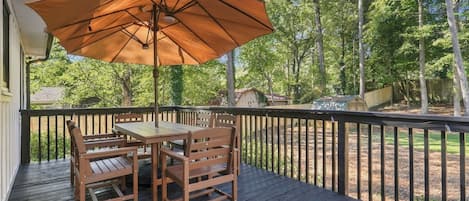 A wooden deck with a table and chairs, an umbrella, and a view of a wooded area.