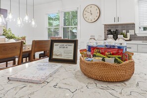 A kitchen with a marble countertop, a framed sign, a wicker basket with snacks, and a clock on the wall. - Modern Gem in the Heart of Alpharetta, minutes to Avalon and HWY 400 (Alpharetta)