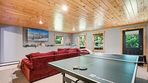 A room with a ping pong table, red sofa, and a TV on the wall. - Peak and Pine Hideway / Hot Tub & Arcade (Bethel)
