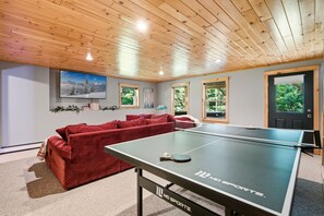 Ein Zimmer mit Tischtennisplatte, rotem Sofa und Fernseher an der Wand.