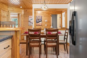 A wooden interior with a dining table, chairs, a refrigerator, and a poster on the wall. - Peak and Pine Hideway / Hot Tub & Arcade (Bethel)