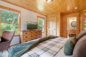 Een slaapkamer met houten lambrisering, een bed, een dressoir, een televisie en een stoel.