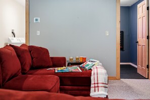 A red sofa, a small table with drinks, and a door leading to another room. - Peak and Pine Hideway / Hot Tub & Arcade (Bethel)