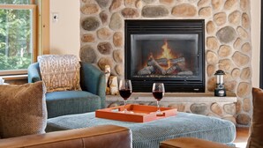 A stone fireplace with a fire, a cozy seating area with a patterned rug, and two glasses of red wine on a tray. - Peak and Pine Hideway / Hot Tub & Arcade (Bethel)