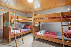Ein Zimmer mit zwei Etagenbetten, einer Holzleiter und einem Fenster mit Blick auf Grünflächen.