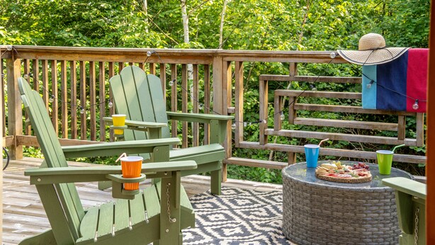 A wooden deck with Adirondack chairs, a wicker table with food and drinks, and a hat on a chair. - Peak and Pine Hideway / Hot Tub & Arcade (Bethel)