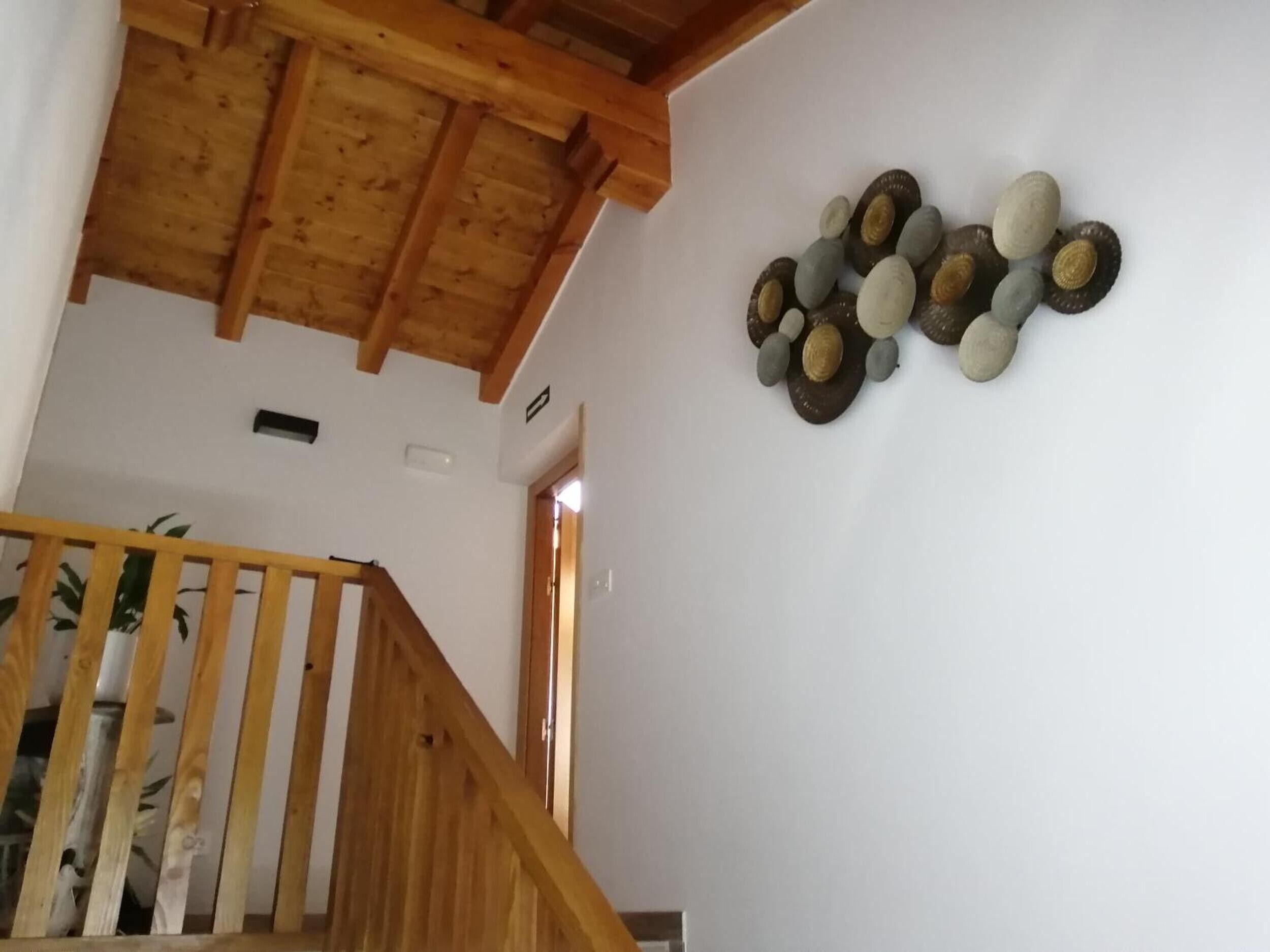 Una scala in legno con corrimano, una parete bianca decorata con conchiglie e un soffitto con travi a vista.