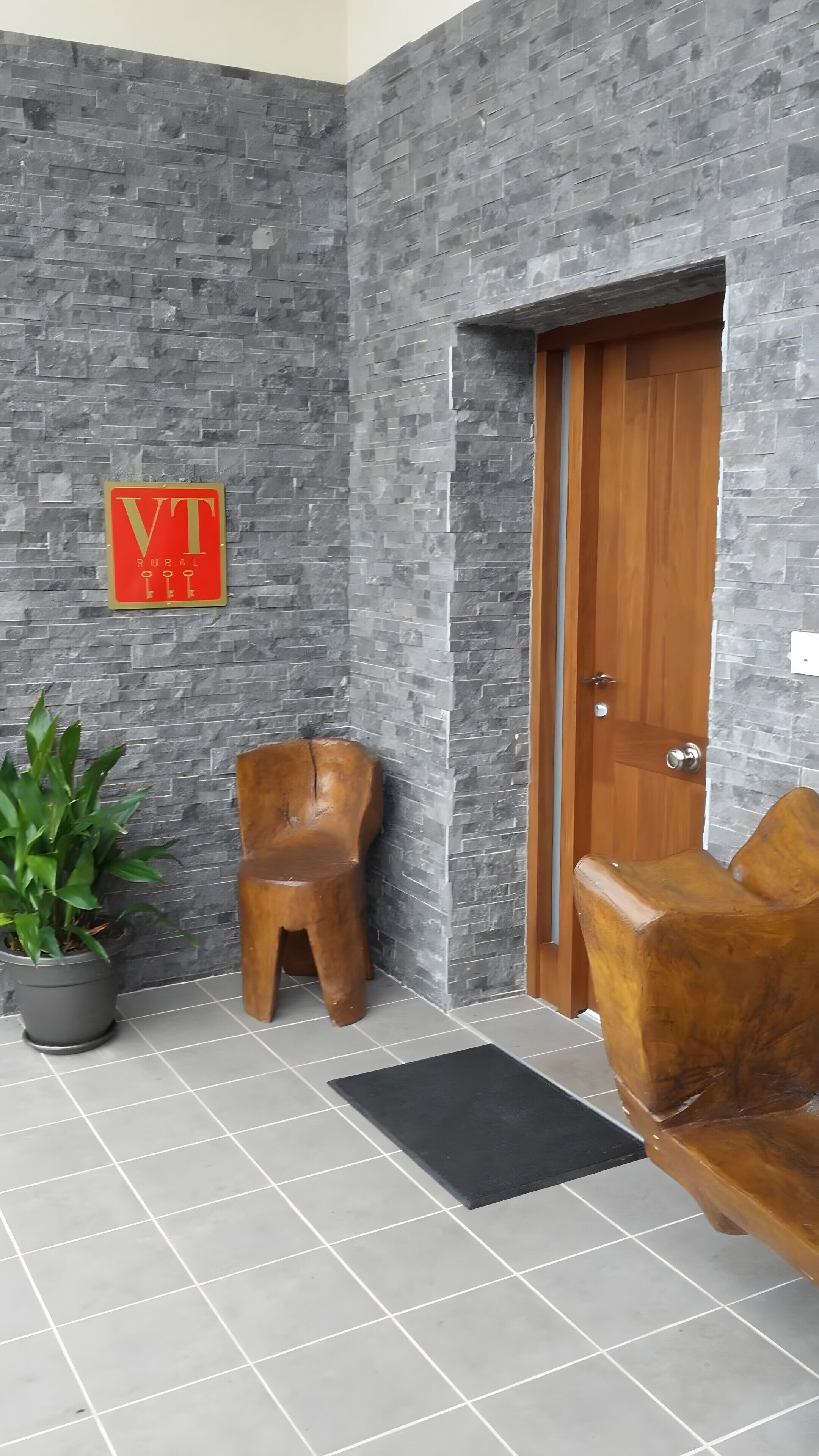 Een receptiegedeelte met een stenen muur, een houten deur, een potplant en twee houten stoelen.