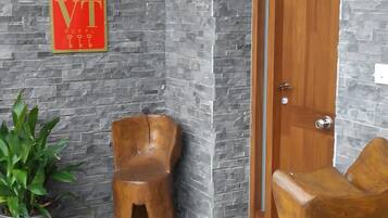 Een receptiegedeelte met een stenen muur, een houten deur, een potplant en twee houten stoelen.