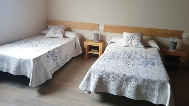 A room with two beds, wooden headboards, and a nightstand with a lamp.