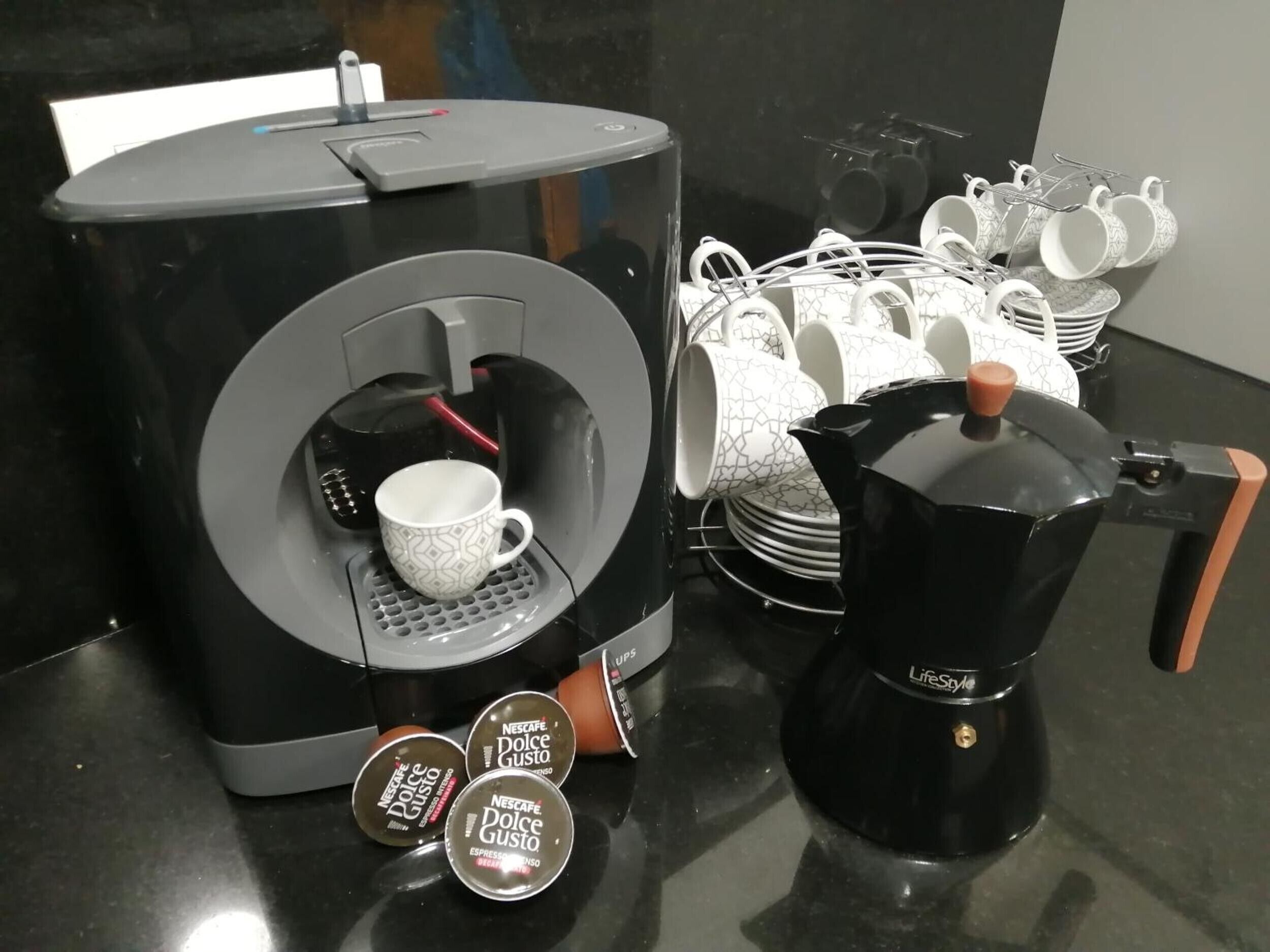 Une machine à café dotée d’un porte-tasse, d’une cafetière et d’une pile de tasses à café.