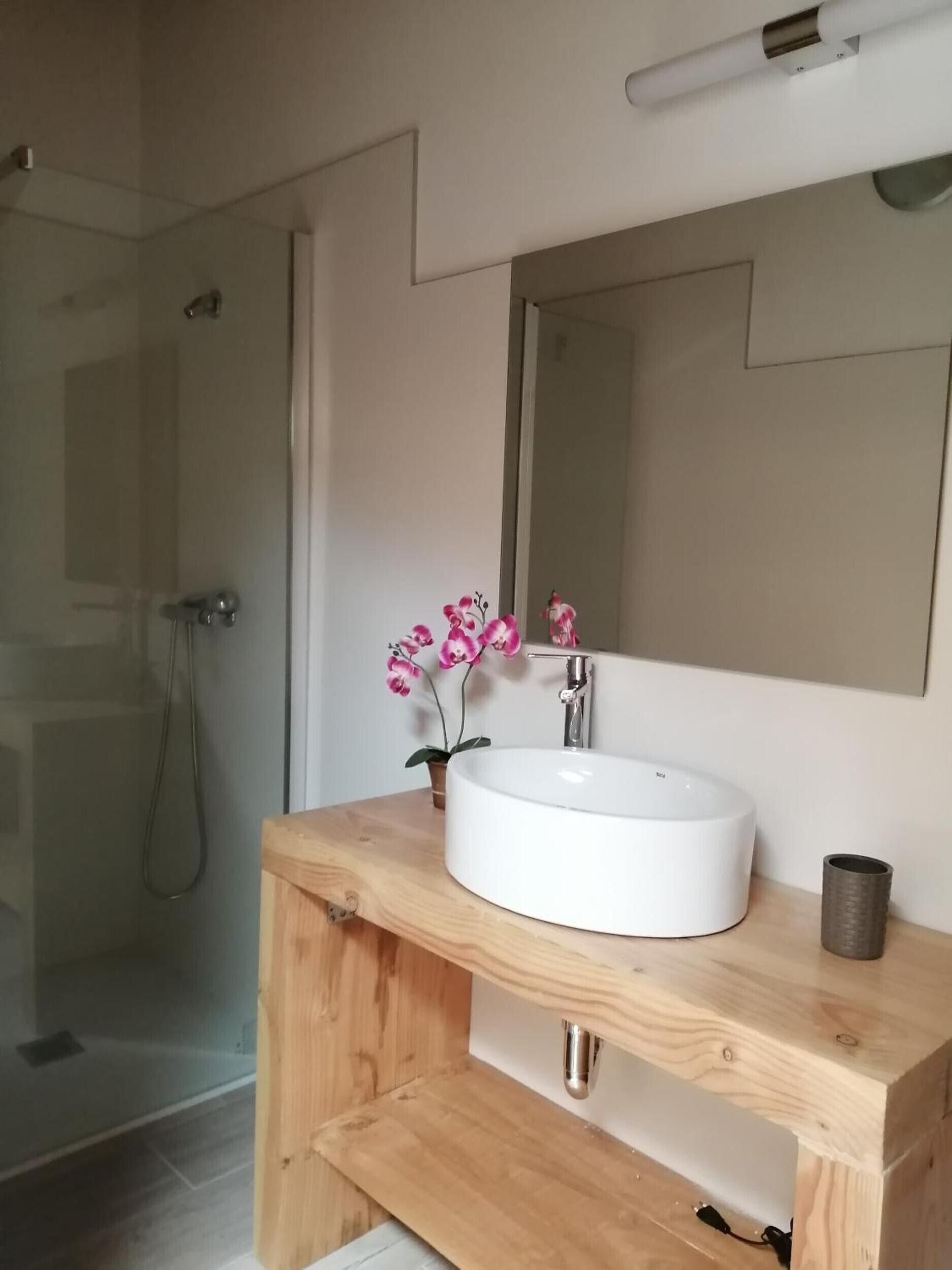 A bathroom with a white sink, a wooden vanity, a mirror, and a shower area.