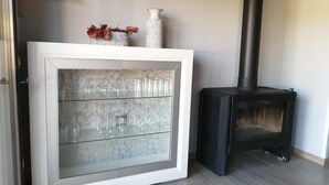 A room with a glass-fronted cabinet, a black wood-burning stove, and a shelf with decorative items.