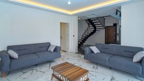 Una sala de estar moderna con dos sofás grises, una mesa de centro de madera y una escalera que conduce a un nivel superior.
