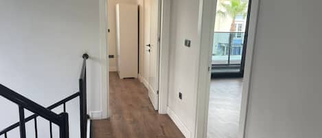 Um corredor com piso de madeira, paredes brancas e corrimão preto.