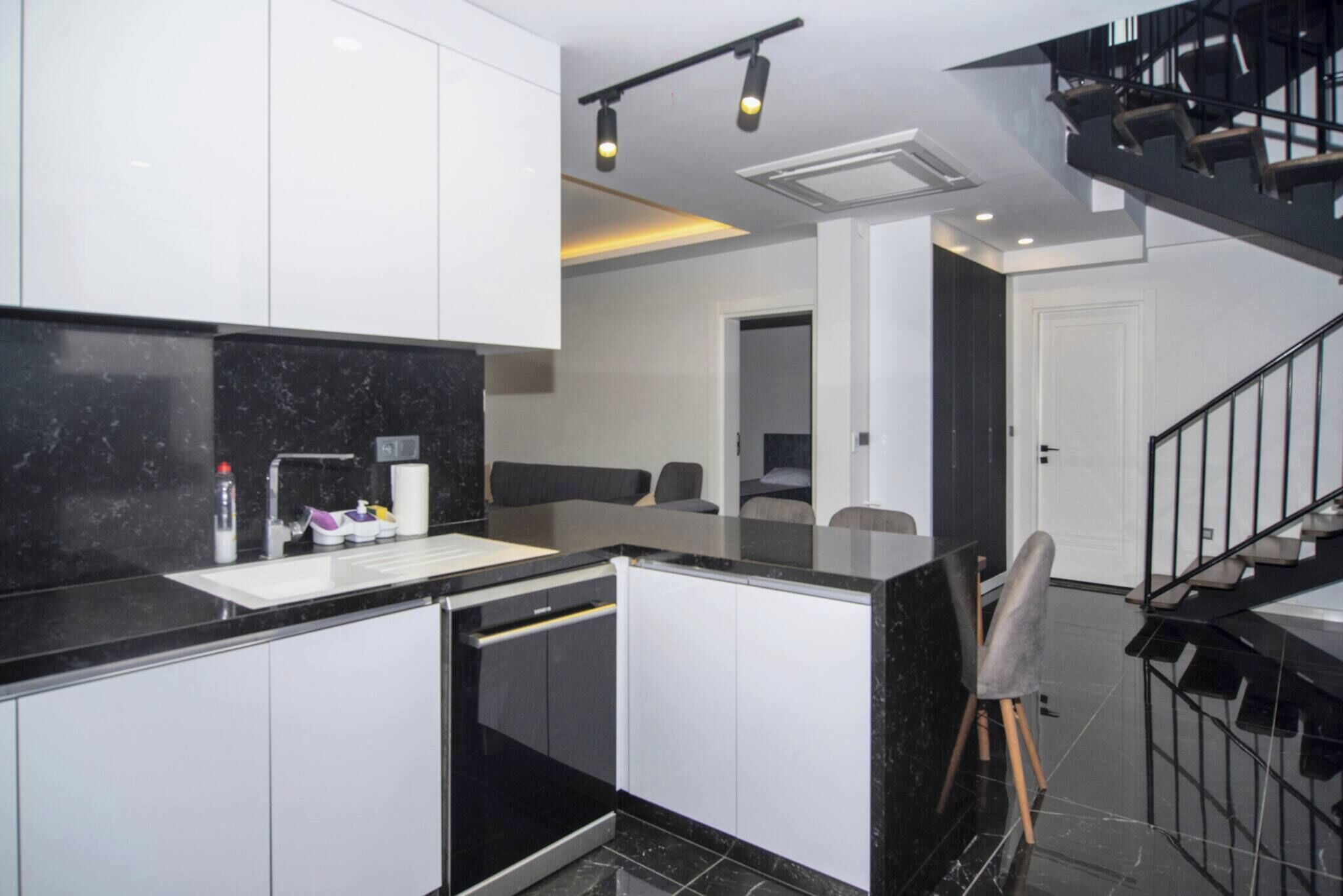 A modern kitchen with white cabinets, a black countertop, and a built-in dishwasher.
