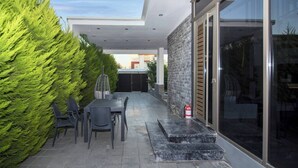 Un patio exterior moderno con una mesa, sillas, un extintor y un portón de vidrio que da a un espacio interior.