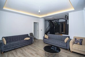 Een moderne woonkamer met twee banken, een salontafel en een trap naar een verdieping erboven.