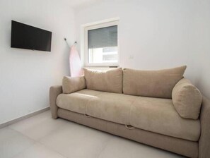 A beige sofa in a room with a flat-screen TV mounted on the wall, a window with blinds, and a tiled floor. - Apartment Alisa, Liznjan: A modern apartment with a sea view (Marčana)