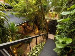 A staircase surrounded by lush greenery, leading to a covered outdoor seating area with a stone wall and a black gate. - 71 HAUS (Medellín)