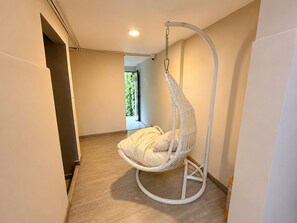 A room with a hanging chair, wooden flooring, and a window with a view of greenery. - 71 HAUS (Medellín)