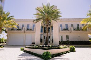 A building with a central palm tree, two-story structure, and a gated driveway. - Casa Playa, Las Iguanas CapCana (Punta Cana)