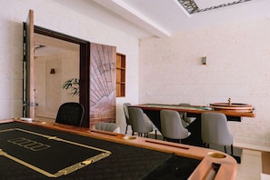A pool table with a wooden frame and a black felt surface with a gold design. There are four chairs around the table. - Casa Playa, Las Iguanas CapCana (Punta Cana)