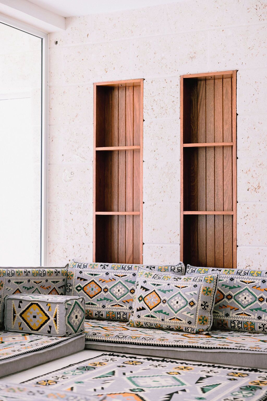 A room with a built-in wooden bench with storage compartments and a patterned cushion.