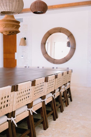 A dining area with a long wooden table, wicker chairs, and a round mirror on the wall. - Casa Playa, Las Iguanas CapCana (Punta Cana)