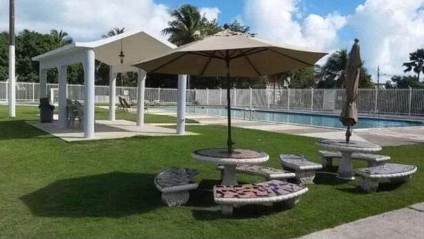 En pergola, utomhusmöbler, en pool och dekorativa stenplanterare.