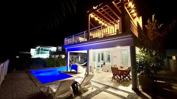 A two-story house with a swimming pool, outdoor seating, and a covered patio area.