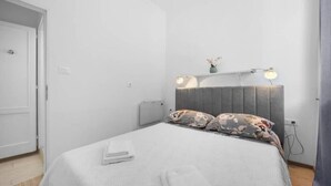 Ein modernes Schlafzimmer mit grauem Kopfteil, zwei Nachttischlampen, einem blumigen Kopfkissen und einem ordentlich bezogenen Bett.