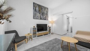 Ein modernes Wohnzimmer mit Flachbildfernseher, einer Couch, einem Couchtisch und einer Lampe.