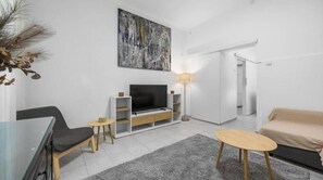 Ein modernes Wohnzimmer mit Flachbildfernseher, einer Couch, einem Couchtisch und einer Lampe.