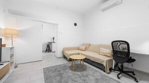 A modern living room with a sofa, a small round table, a black office chair, and a lamp.