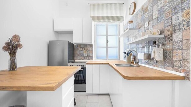 Eine moderne Küche mit weißen Schränken, einer Holz Arbeitsplatte und einer Spritzschutzleiste mit gemusterten Fliesen.