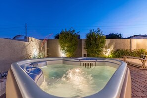 A hot tub in a backyard with a table and chairs, surrounded by plants and a brick wall. - Epic PHX Fun-Game Room•Pool•Hot Tub•Mtn Views (Phoenix)
