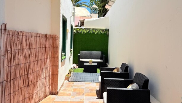 Eine schmale Außenpatio mit Fliesenboden, einer Sitzecke mit dunklen Korbmöbeln und einer grünen Wand.