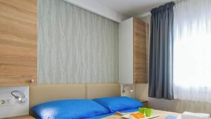 Ein Hotelzimmer mit Bett, Nachttisch, Lampe und einem Fenster mit Vorhängen.
