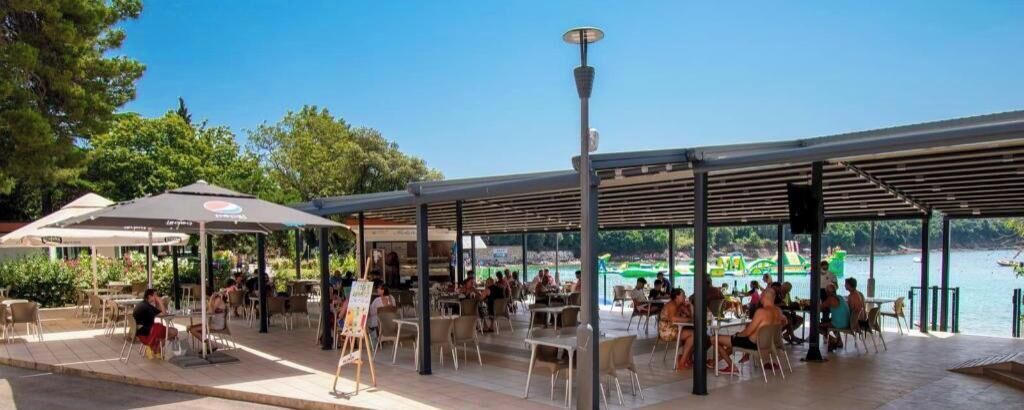 Een terras met tafels en stoelen, een overdekt zitgedeelte, en uitzicht op het water.