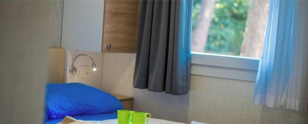 Een slaapkamer met een bed, nachtkastje, lamp en een raam met gordijnen.