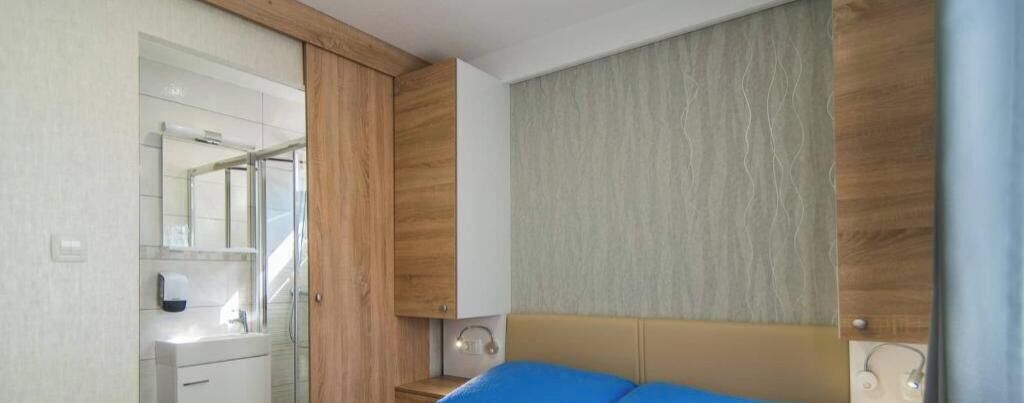 A bedroom with a bed, a nightstand, a mirror, and a wooden wardrobe.